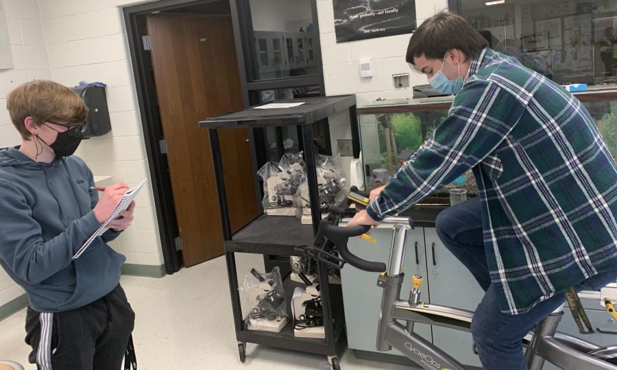 On the left junior Jeremy Disterhaft takes notes while right, senior Sam Petraszak, rides a stationary bike to test a hypothesis. Petraszak was a test subject for Disterhaft’s Advanced Biology project. “I think they were trying to see if physical activity changes a persons reflex time,” Petraszak said.