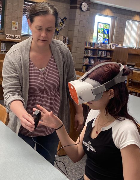 Library media specialist Sarah Gumtow and sophomore Adeline Voigtlander test out the VR headset in the LMC. “The VR headsets could be used to help students visualize concepts that are really hard to visualize otherwise,” Gumtow said. “I think that they’ll be able to really enhance some of the things that teachers are already doing.”
