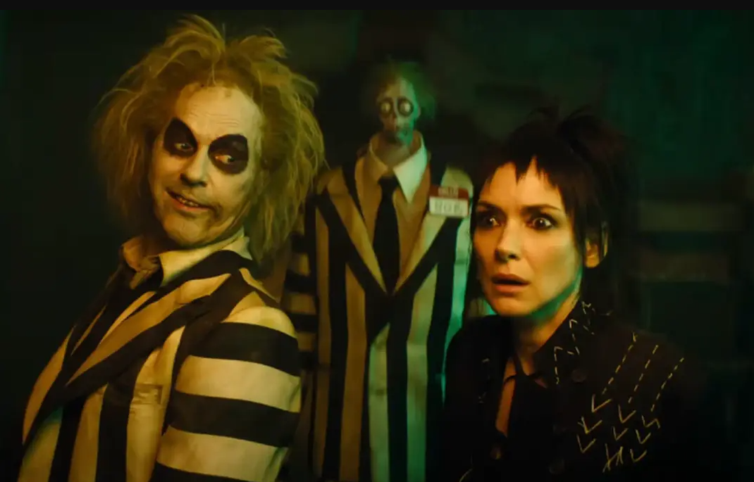 Beetlejuice (Michael Keaton) (left) and Lydia Deetz (Winona Ryder) (right) reuniting after many years apart, with Beetlejuice’s goon Bob (Nick Kellington) (back) watching them. 
