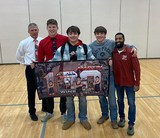 Left to right: Fourth-grade teacher and former coach Scott Wagner, wrestling coach Beau Yineman, senior Jakob Martin, Ethan Zache, and wrestling coach Dobs. Martin presents a banner portraying his 100-win accomplishment, with a collage of photos illustrating his many triumphs. 

